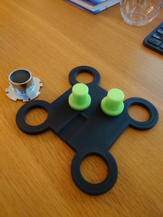 Svart prototyp med fyra öppningar och tre gröna kopierhylsor insatta på ett bord, bredvid en metallbit.