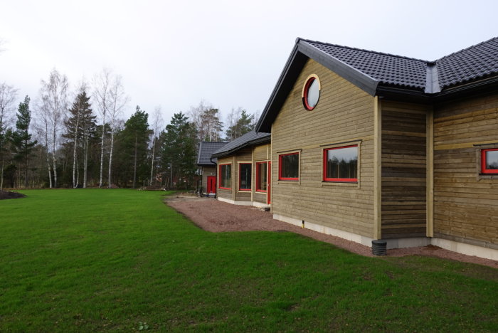 Ett nybyggt hus med ljusslinga och gräsmatta, omgivet av skog i dagsljus.