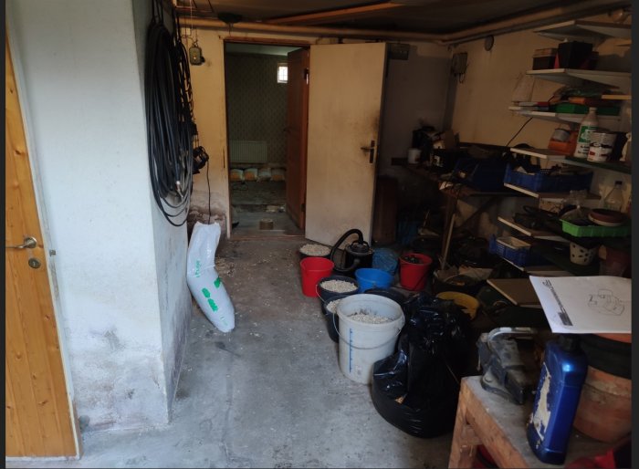 Oorganiserad källare med betonggolv och diverse byggmaterial före renovering.