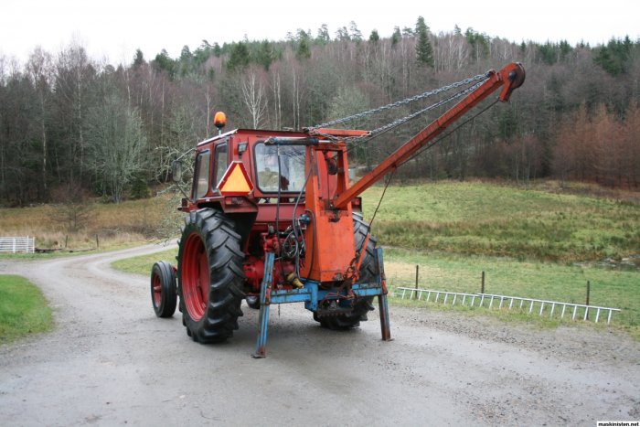 Röd veterantraktor med kran och skog i bakgrunden.