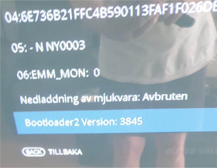 Bild på en elektronisk skärm som visar firmware info, inklusive "Bootloader2 Version: 3845", med en spegling av en person.