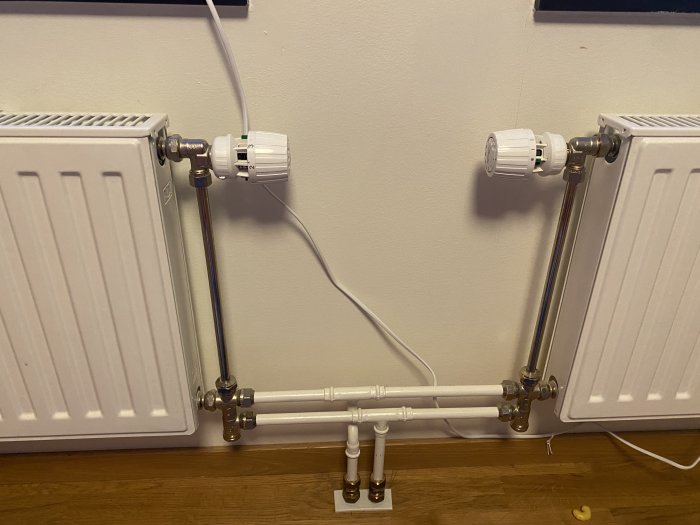 Två radiatorer med ställdon kopplade till gemensamma rör på en vägg.