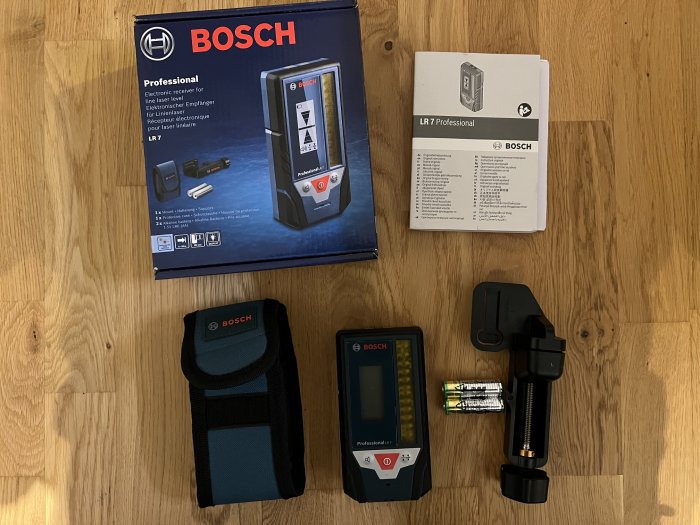 Bosch GLL 3-80 CG laser och LR7-mottagare med tillbehör och manualer på trägolv.