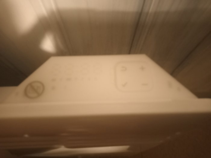 Otydligt foto av en vit värmeelementstermostat med digitala knappar för inställningar