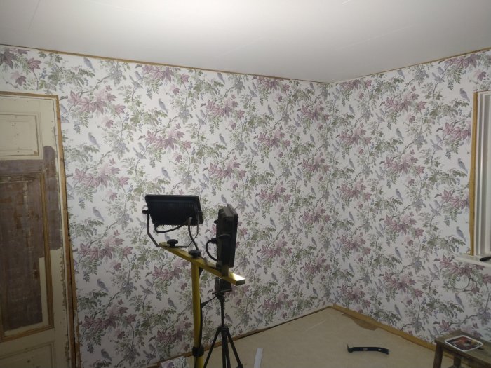 Ett rum med nytapetserade väggar i blommigt mönster och arbetarbelysning på golvet.