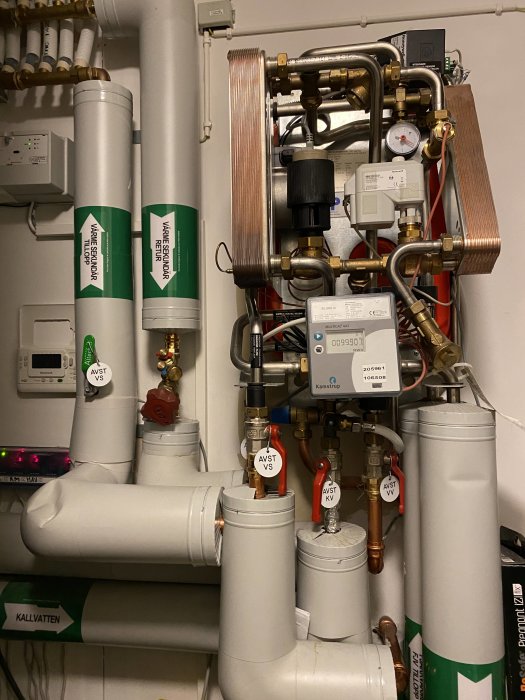 Värmesystem med rör, ventiler märkta "AVST VS" och mätutrustning i ett pannrum.