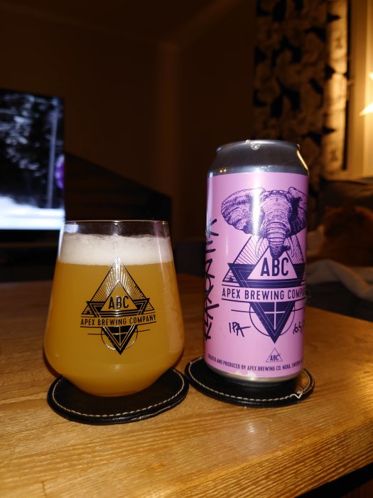 Ölglas med skum från Apex Brewing Company och en ölburk med etiketten "Beaks and Talons" på ett träbord.