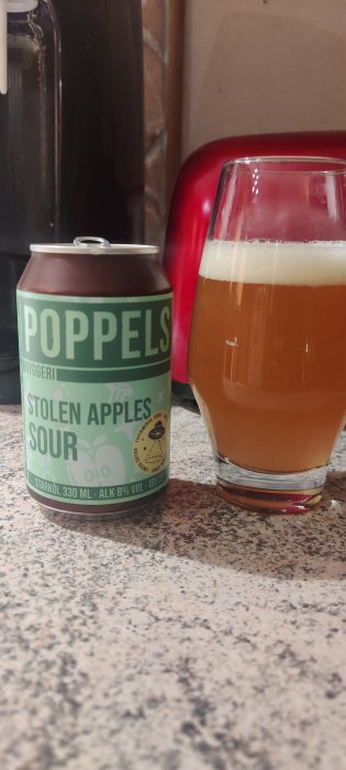 Burk Poppels Stolen Apples Sour bredvid ett glas öl på en bänkskiva.
