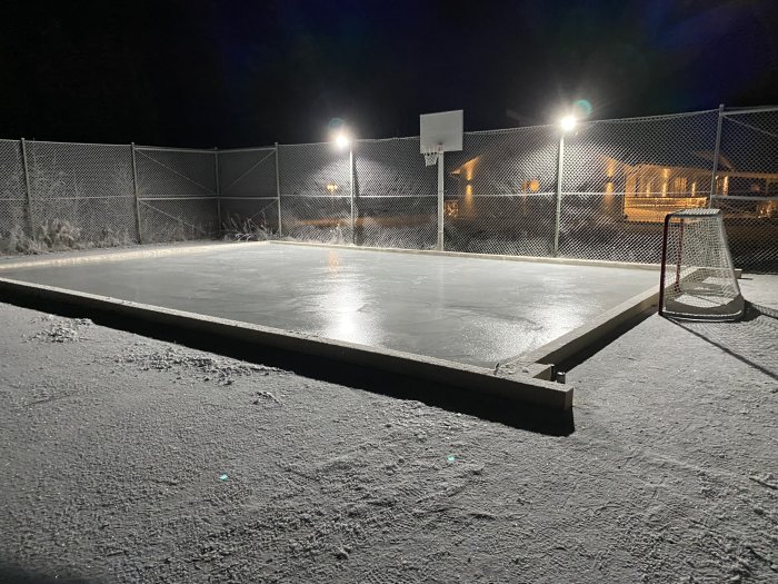 Ishockeyrink med nyligen fryst is och sprickor, belysning i bakgrunden och målbur till höger.