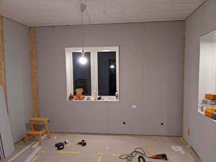 Vägg med nyinstallerade gipsskivor och verktyg på golvet i ett pågående renoveringsprojekt.