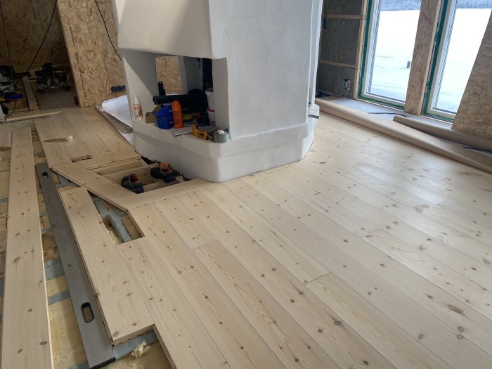 Delvis lagt trägolv i rum med öppen spis och synliga verktyg, arbete i process.