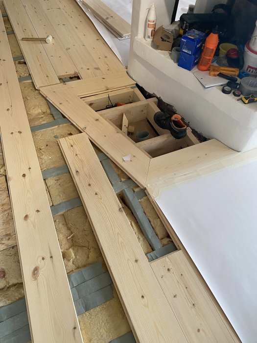 Ny lagd trägolv runt en öppenspis och i en hall med verktyg och byggmaterial synliga.