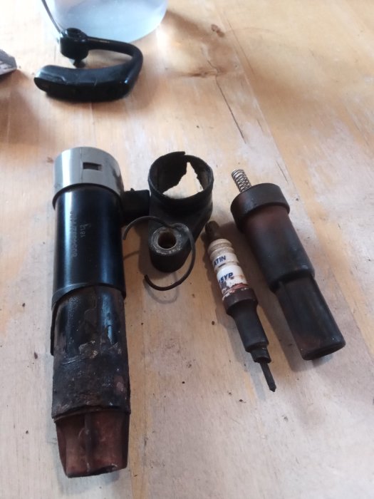 Exploderad tändspole och trasigt tändstift på en träbakgrund, bilreparationsdelar.