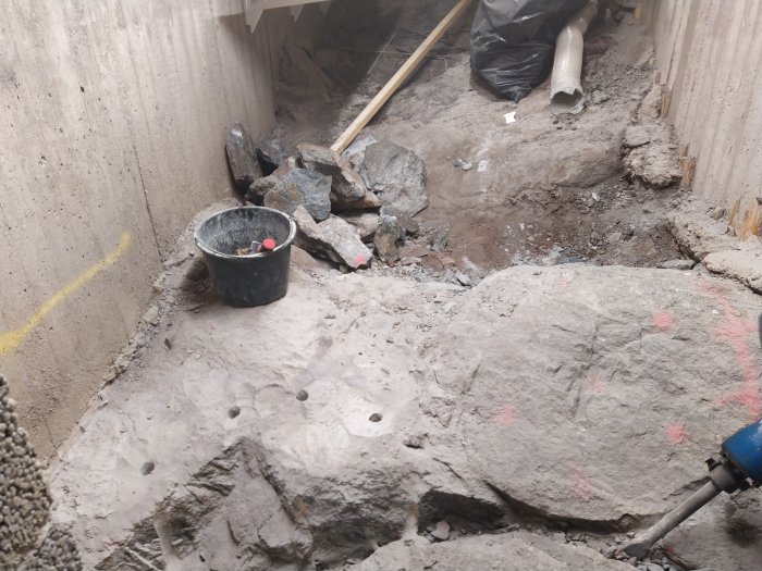Bild av en byggarbetsplats med en pneumatisk borr, spräckta stenblock och borrade hål i berggrunden.
