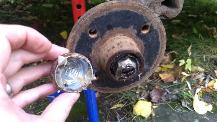 Hand som håller en demonterad hjulmutter framför ett hjulnav med synliga inbuktningar och packning.