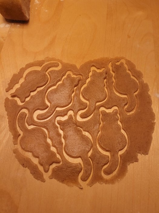 Pepparkaksdeg med utstansade figurer av katter och ekorrar på ett träbord.