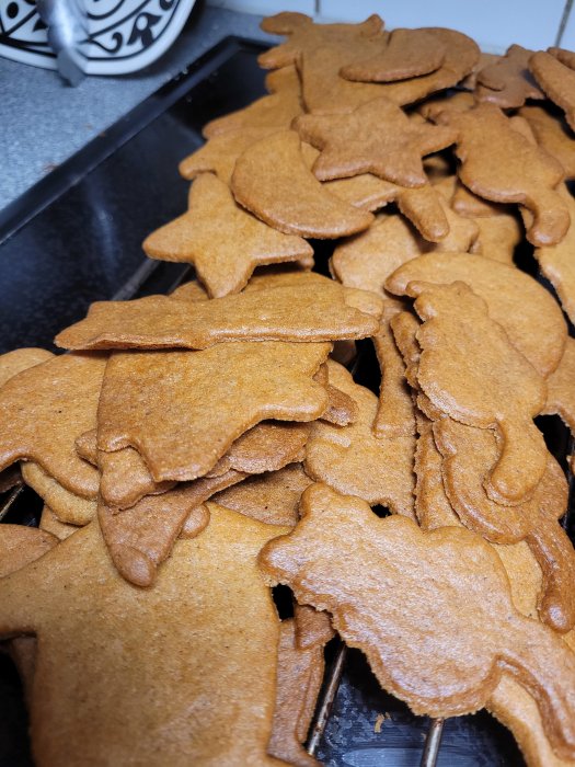 Nybakade pepparkakor i olika former staplade på ett köksbord.