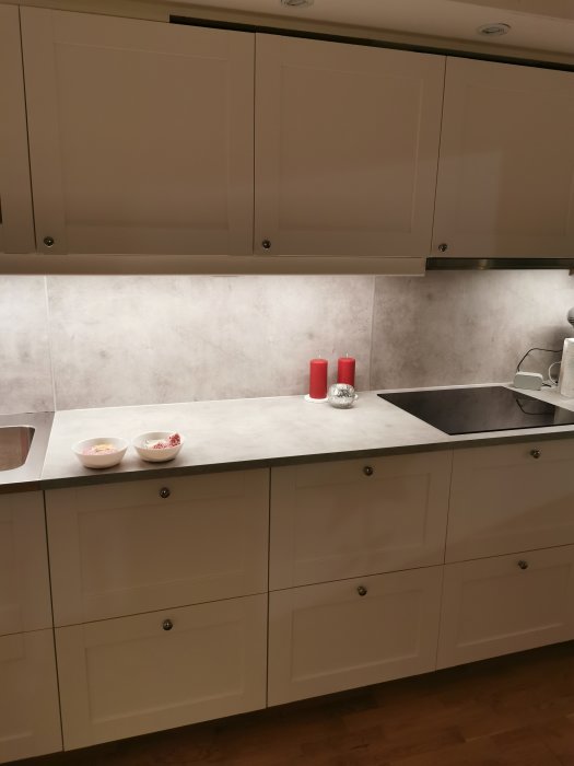 Kök med vita lådfrontar och skåp med knoppar, marmorbänkskiva och två röda ljus.