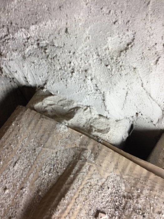 Dammigt murbruk runt en ej synlig eternitkanal i en murstock under en renoveringsprocess.