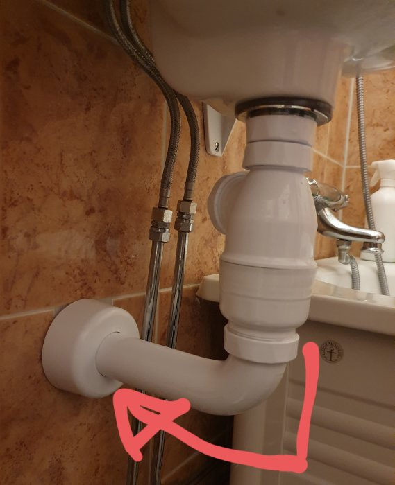 Handfatets VVS-installation med rör och vattenlås som är snett monterat och icke-centrerat i förhållande till väggen.