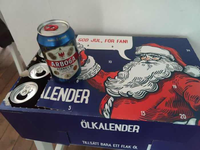 Ölkalender med julmotiv och en öppnad lucka som visar en burk starköl, samt flera tomma burkar ovanpå.