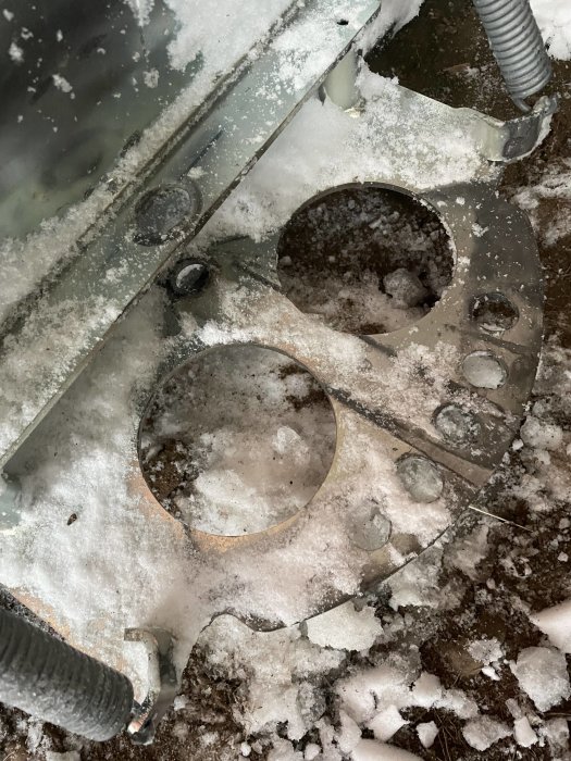 Metallfäste till plog med 20 mm hål och skadade delar, täckt av snö.