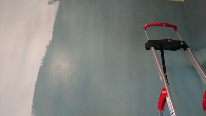 Hörn av ett rum med väggar delvis målade i vitt, en stege framför väggen.