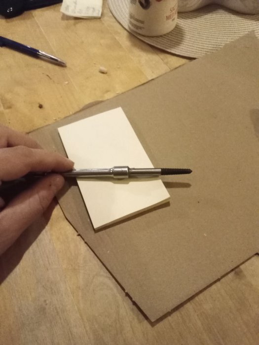 Hand håller en grispitt (skruvutdragare) med ett limmat handtag av träblock på ett bord.