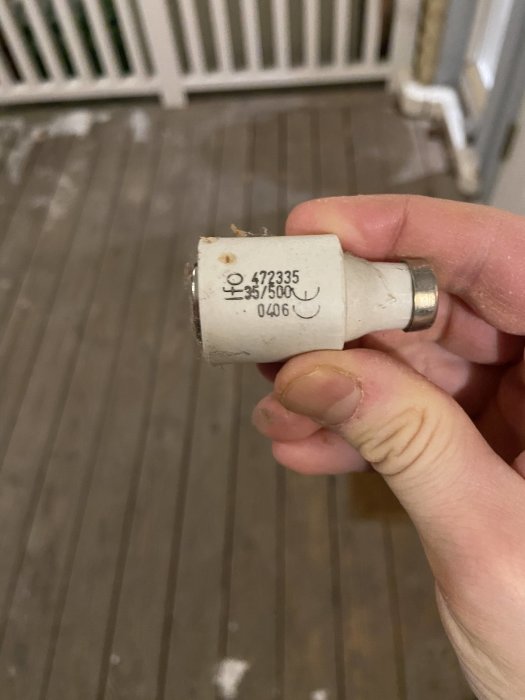 Hand håller en säkring märkt med "35A/500V" i ett rum som kan ha varit hobbyverkstad.