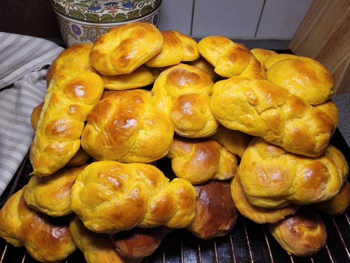 Nybakade saffransbullar i en stor hög på ett köksställ, med en handduk och burk i bakgrunden.