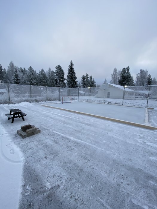 Hemmagjord isrink med slät yta på 10 cm is, inramad av stängsel i ett vinterlandskap.