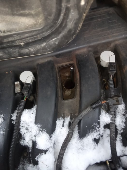 Batterifack i en bil med synlig korrosion och snö omkring kablar och komponenter.