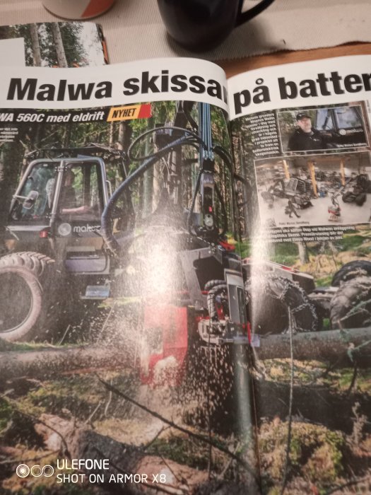 Tidningssida om Malwa skogsmaskin 560C med eldrift som kapar en trädstock i skogsmiljö.