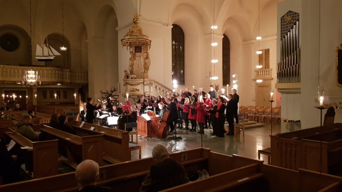 Orkester och kör uppträder under en konsert inne i en kyrka med publik i bänkarna.