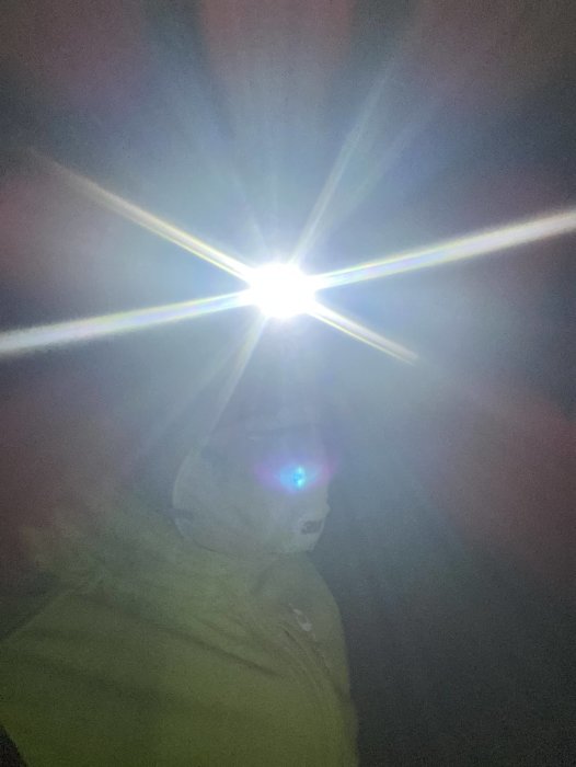Person med pannlampa i mörker, starkt ljus från lampan orsakar linsflare-effekt.