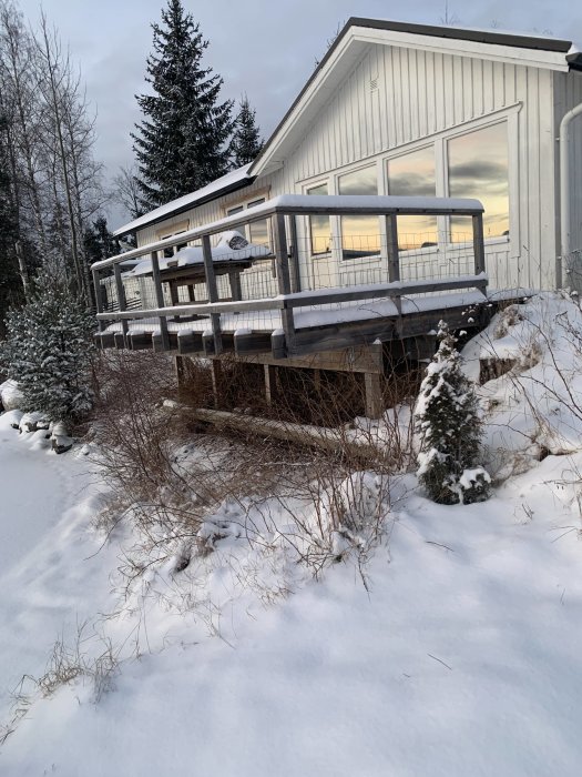 Hus med altan utan glas och med nät, omgivet av snötäckt mark och barrträd.