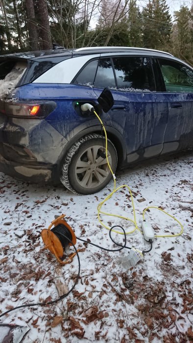 Elbil laddas med förlängningssladd och portabel laddare på en snötäckt mark.