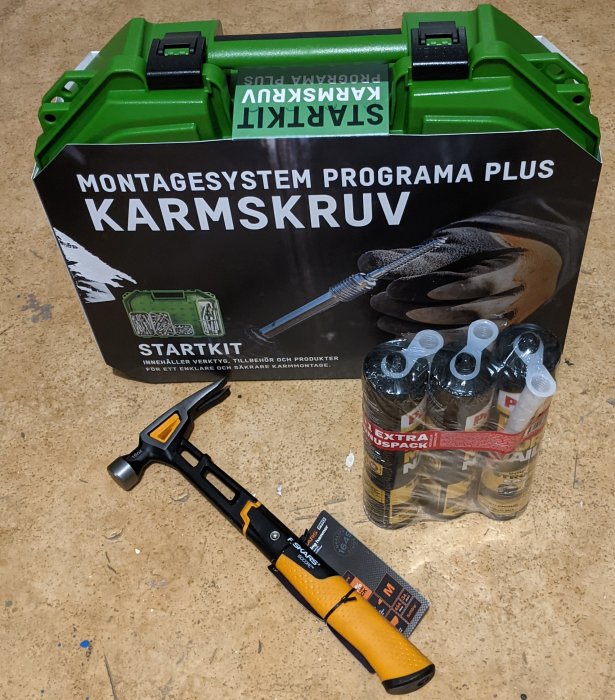 Startkit för montage av karm med skruv, hammare och pack av silikonkartuscher på ett verktygsbord.