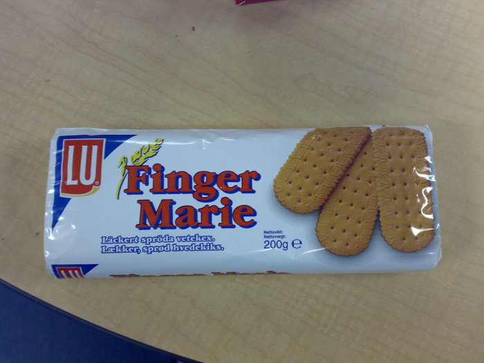 Förpackning av LU Finger Marie-kex bredvid lösa kex på ett bord.