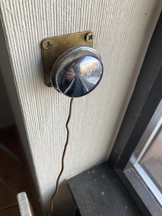Koppartråd ansluten till en äldre termostat monterad på vägg vid fönster, med reflektion av en person.