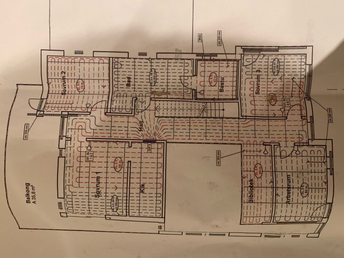 Ritning av ett hus med markerade slingor för vattenburen golvvärme och beteckningar för olika rum som bibliotek och sovrum.
