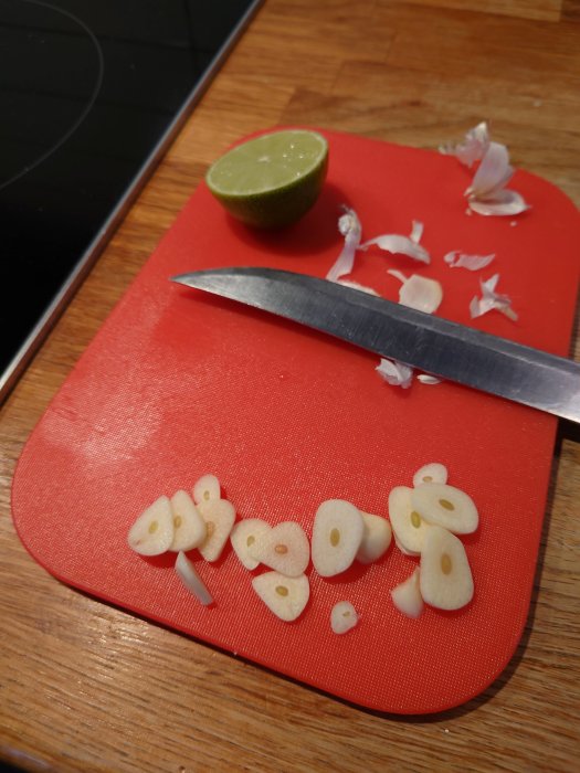 Skärbräda med skivad vitlök, kniv och halverad lime, förberedelse för matlagning.