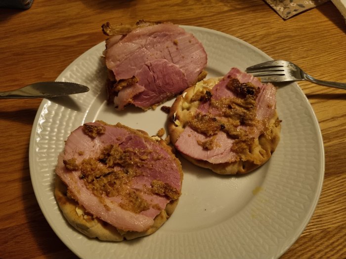 Två rågkakor toppade med rosa julskinka och senap på ett vitt fat, redo för julskinkemackans premiär.