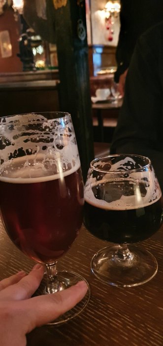 Två ölglas på bord, ett med rödbrun ale och det andra med mörk ale, på en pubmiljö.