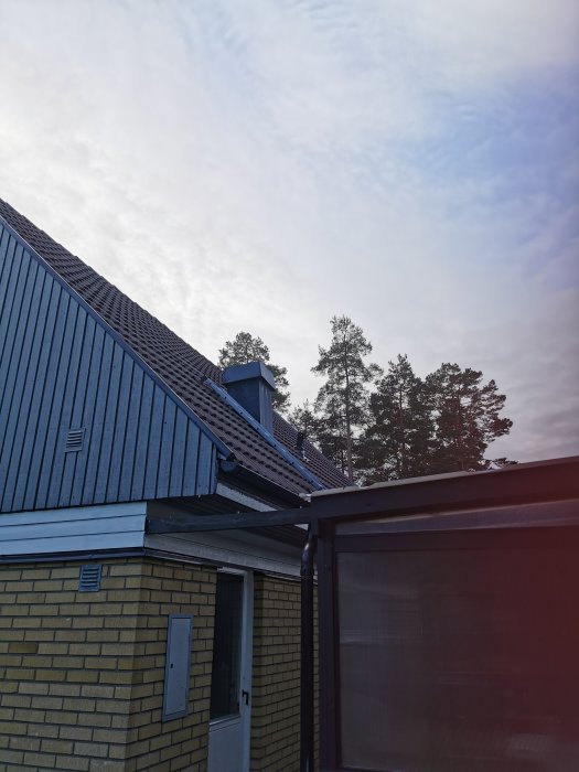 Bild av ett hörn av ett hus med blå betongpannor på taket, tagen på senhösten utan synlig snö.