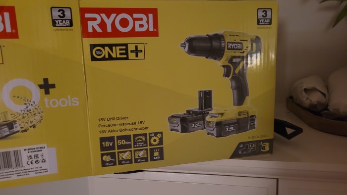 En RYOBI 18V borrskruvdragare i förpackning med två 1.5 Ah batterier, presenterad på en hylla.