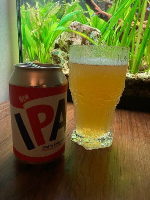 IPA-ölburk bredvid ett glas med grumlig öl framför akvarium med växter.