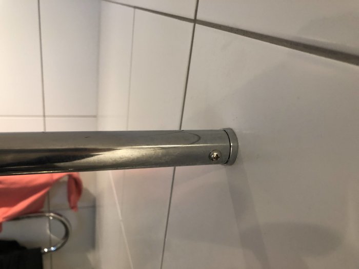 Rör fäst i kakelvägg med skruv och möjlig springa vid fästpunkten som kan vara lim eller spricka.