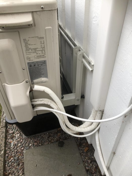 Utedel av en luft-luft värmepump placerad vid en husvägg med synliga rör och kablar.