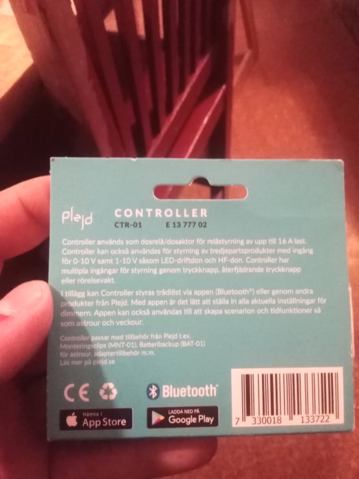 Hand håller en förpackning för en Plejd Controller, med produktinformation och streckkod synlig.
